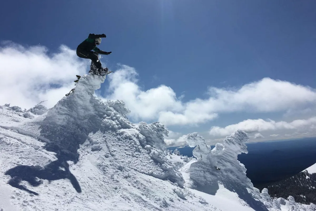 A dynamic image of a snowboarder launching from a snowy peak, surrounded by clouds and dramatic mountain scenery. The action and camaraderie implied by winter sports make it ideal for group-oriented content.