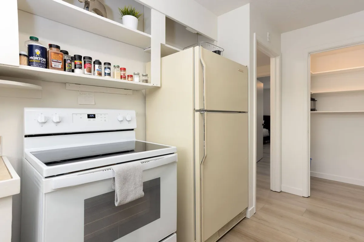 This cozy kitchen image centers on a white stove, cream refrigerator, a well-stocked spice rack, and open shelving. These details suggest a space designed for culinary creativity and comfortable entertaining.