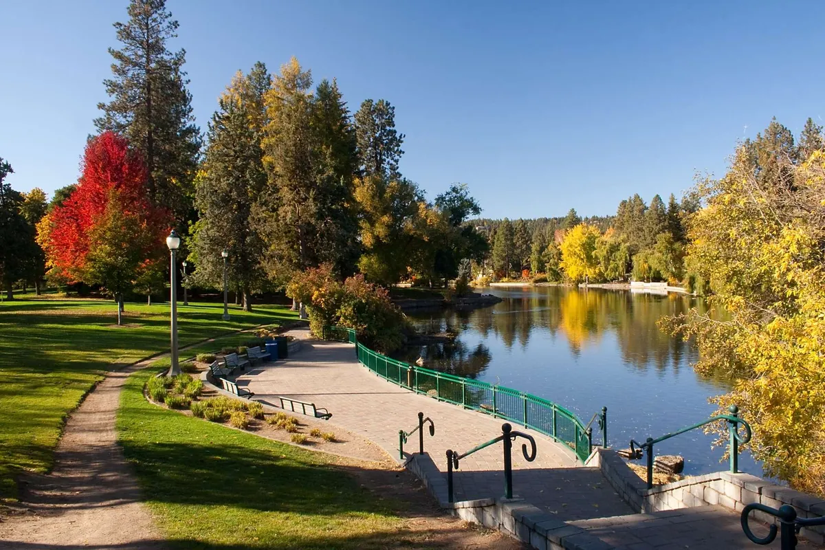 This image captures a scenic lake surrounded by colorful trees, a walking path, park benches, and a small bridge. The peaceful setting invites outdoor activities such as walking, picnicking, jogging, or simply relaxing by the water—a perfect representation of the nearby parks and the family-friendly, nature-oriented neighborhood.