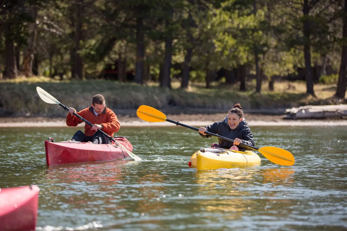 This image features two kayakers gliding across clear water, bordered by a natural shoreline. The water sparkles in the sunlight, and the atmosphere is energetic and adventurous, perfectly capturing the spirit of Bend’s outdoor activities.