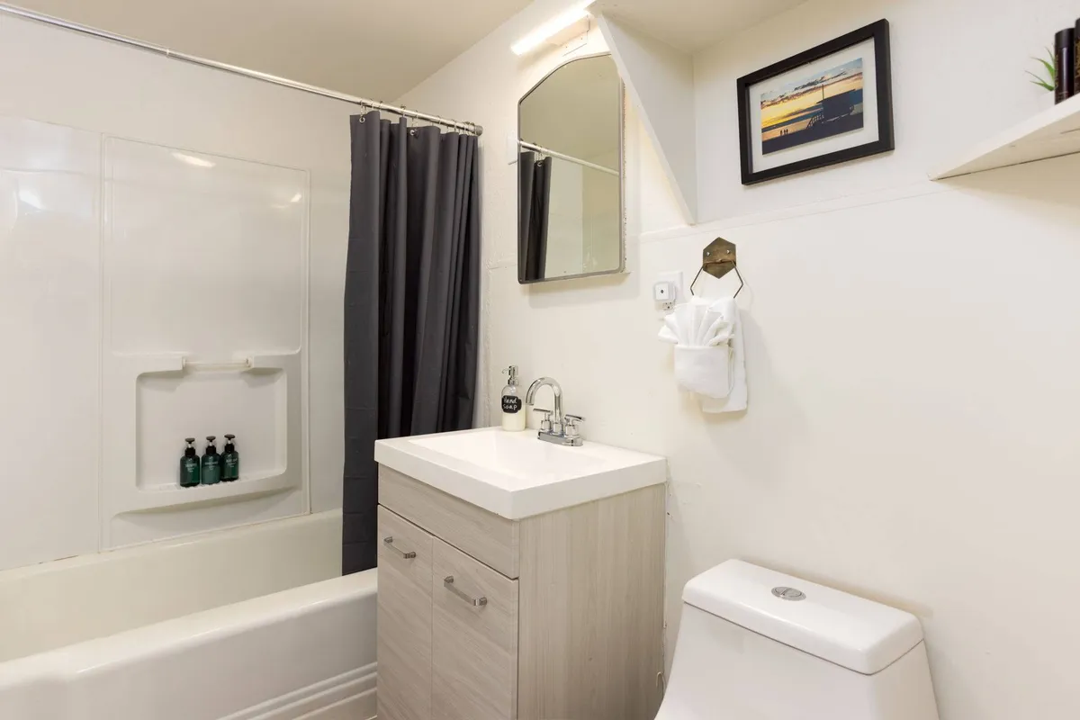 A calm, updated bathroom featuring a vanity with sink, bathtub with shower curtain, large mirror, and framed picture. The scene feels fresh and inviting, ideal for refreshing routines and moments of personal care.