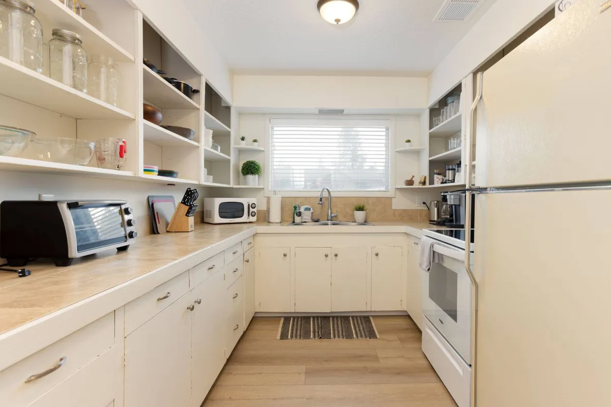 This image showcases the heart of the kitchen, including the kitchen sink, ample counter space, modern shelves, and visible kitchen appliances. The lighting and layout suggest a space designed for cooking and gathering, ideal for group meal prep or baking together.