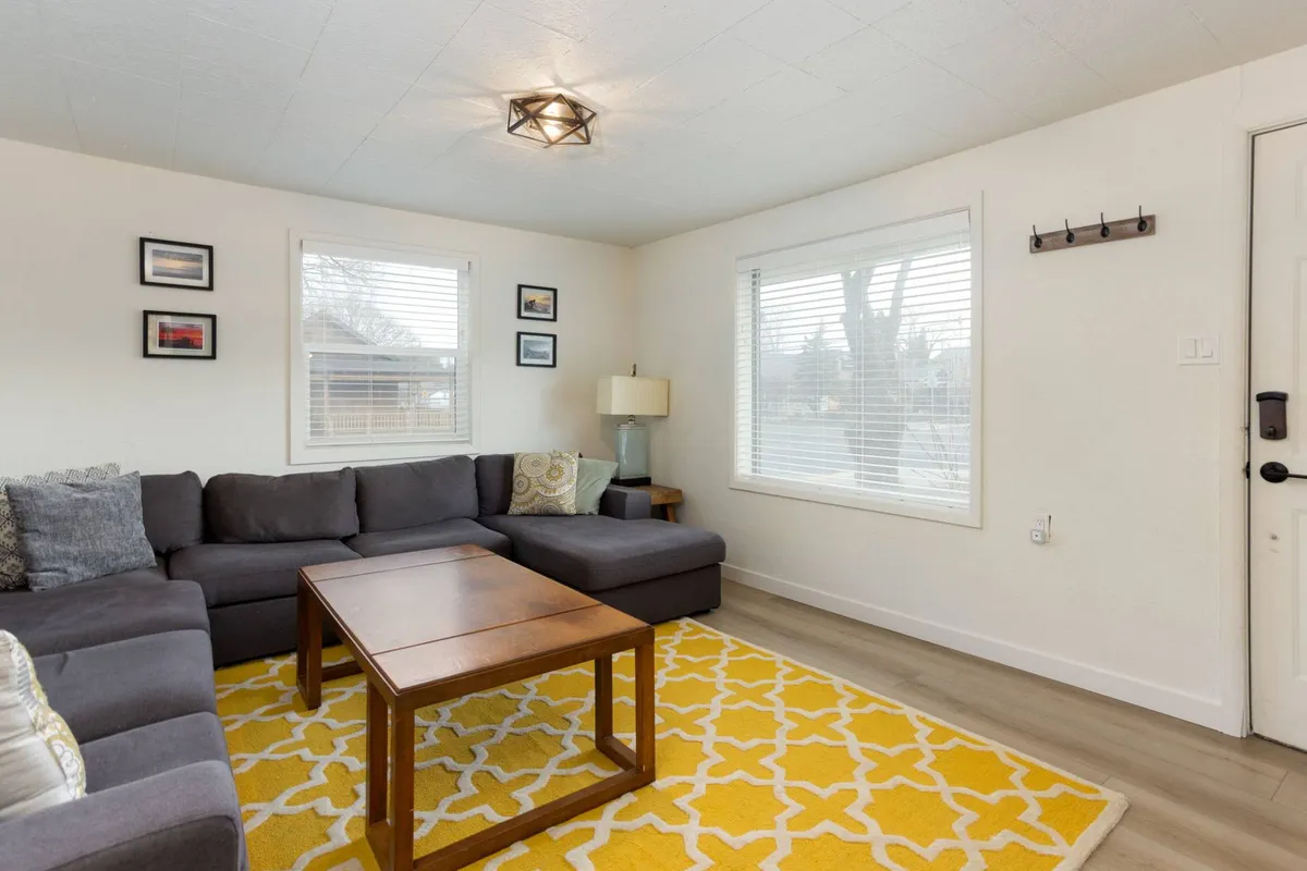 A cozy living area with a plush sofa, coffee table, and ample natural light streaming through the windows. The scene evokes relaxation and socializing after a day out in Bend.