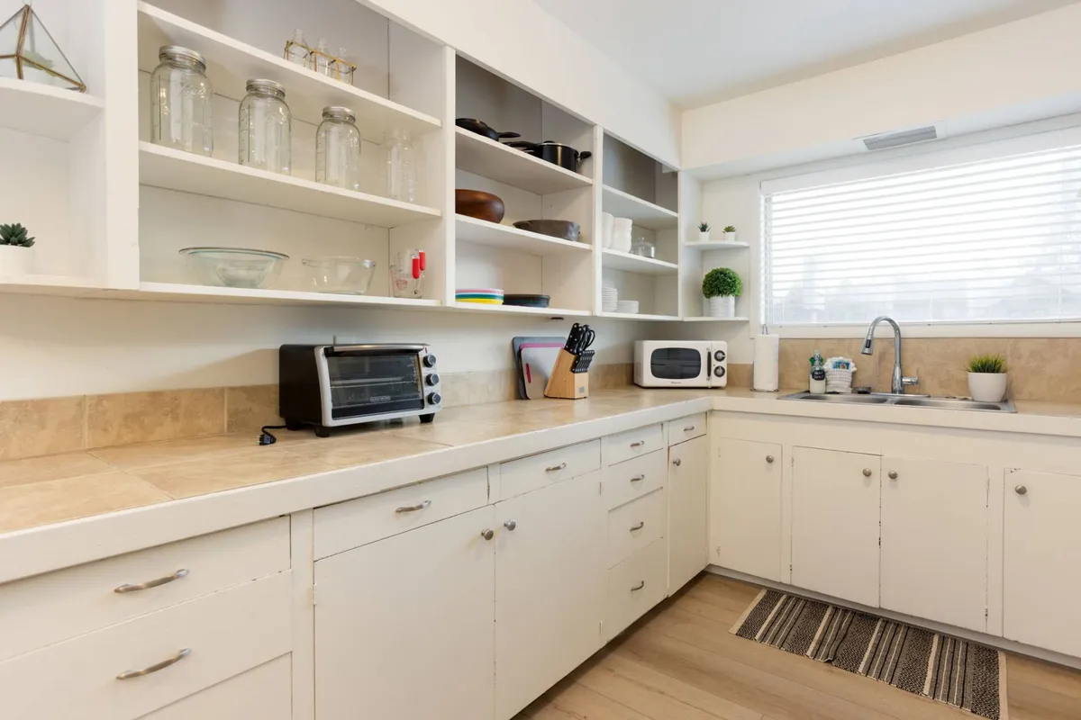 This photo features a bright kitchen countertop, shelves lined with glass jars, a modern sink, and a microwave. The space is organized, inviting, and hints at a well-equipped kitchen ideal for both daily meals and special gatherings.
