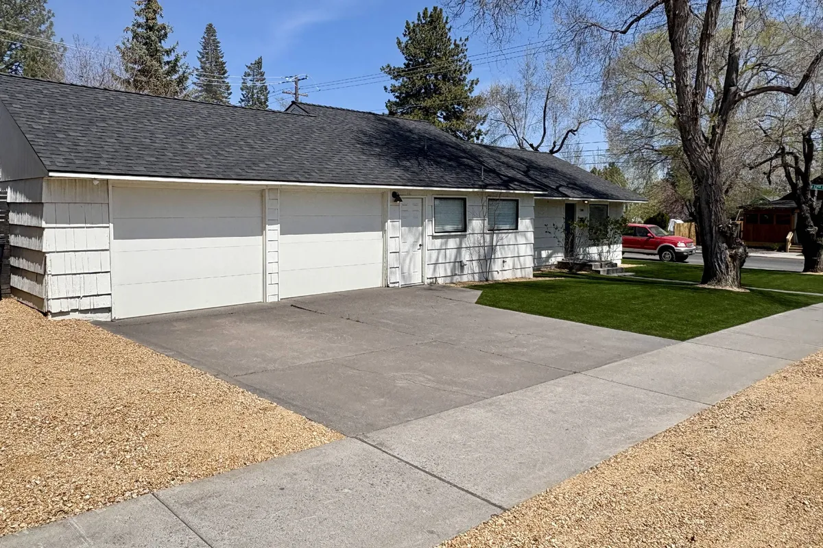 This exterior image showcases the two-car garage of the property, a neatly landscaped lawn, and a gravel driveway. The scene is bright and inviting, suggesting a welcoming entry point and an appealing outdoor space that hints at the walkable neighborhood just beyond.