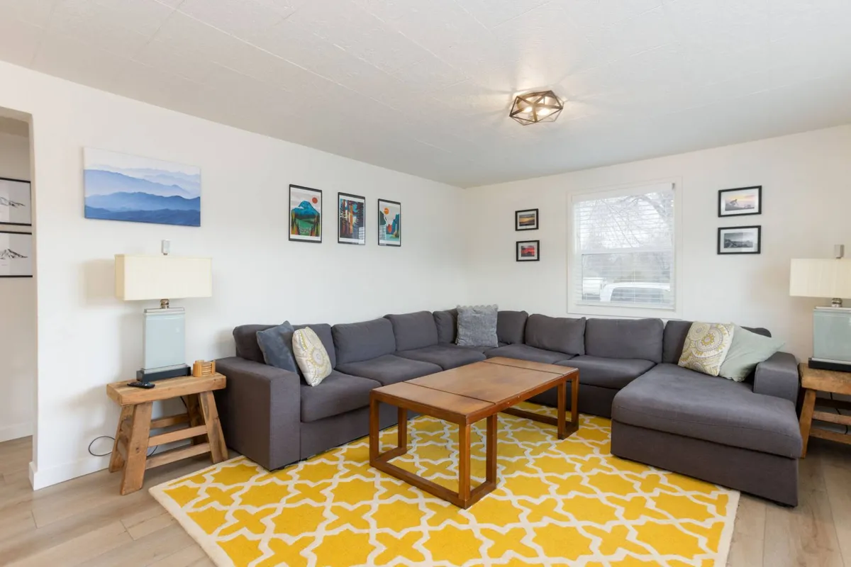 A spacious living room featuring a large sectional sofa, a colorful area rug, a central coffee table, and stylish wall art. The setup invites relaxation and socializing, with ample seating and a cozy atmosphere created by the soft textures and vibrant decor.